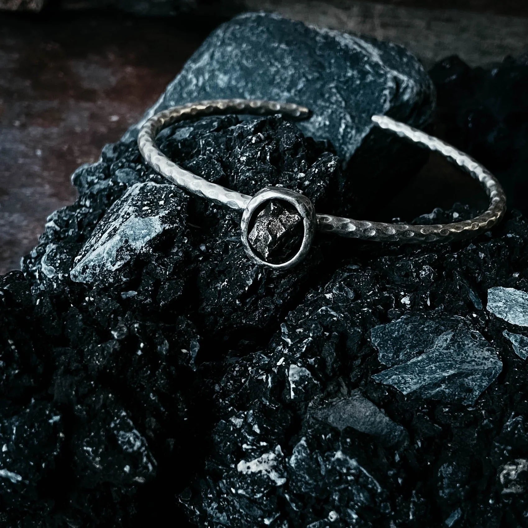 Handcrafted silver bracelet with a dark crystal centerpiece on black rocky stones, Qu!rk Boutique