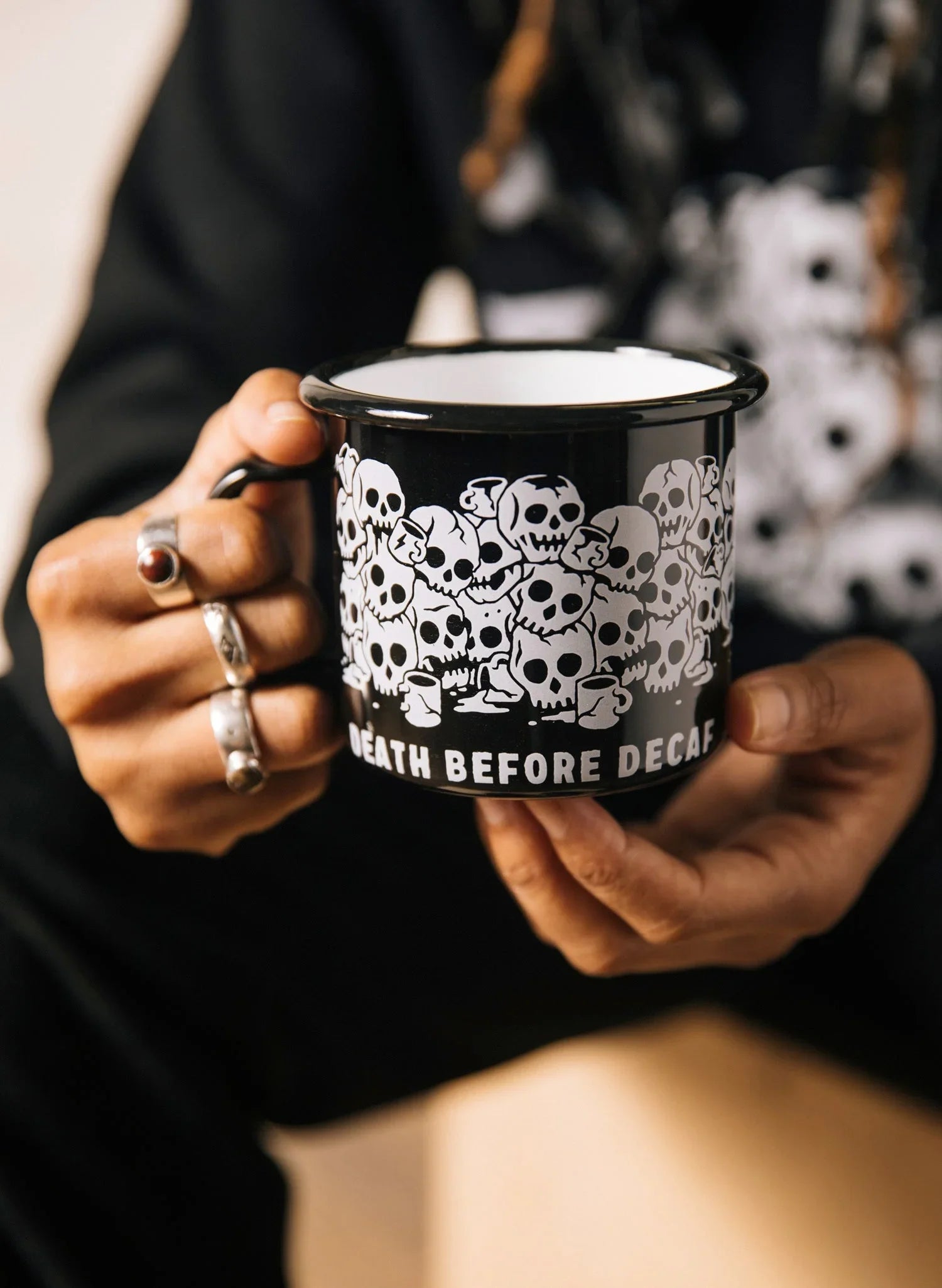 Black enamel mug with white skull design and 'Death Before Decaf' text, held in hands, Qu!rk Boutique