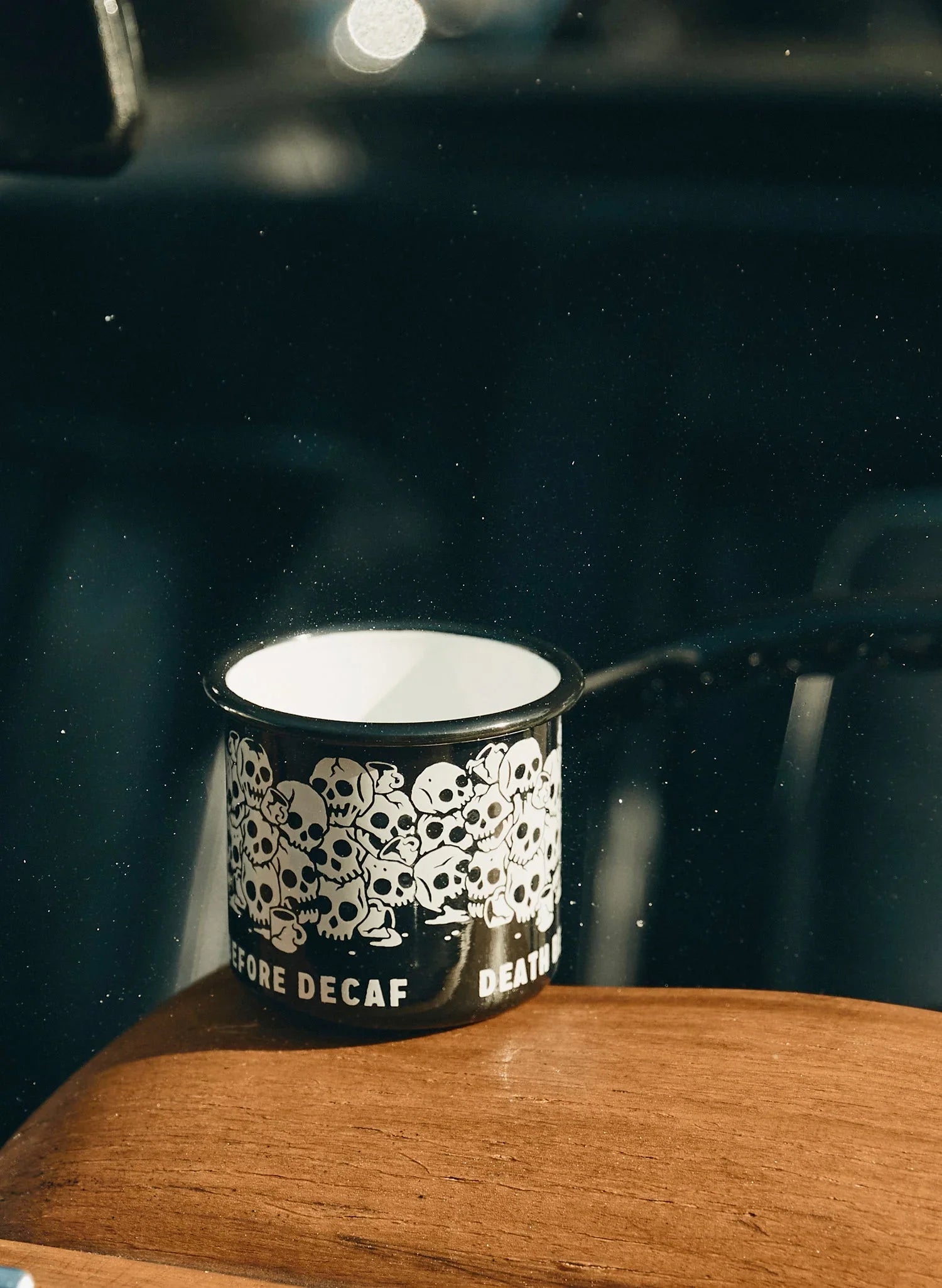 Black enamel mug with white skull pattern and 'Death Before Decaf' text on wood surface