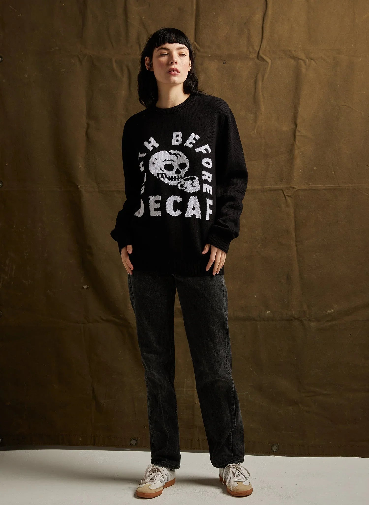 Woman wearing black sweater with skull and 'Death Before Decaf' text, black jeans, and sneakers