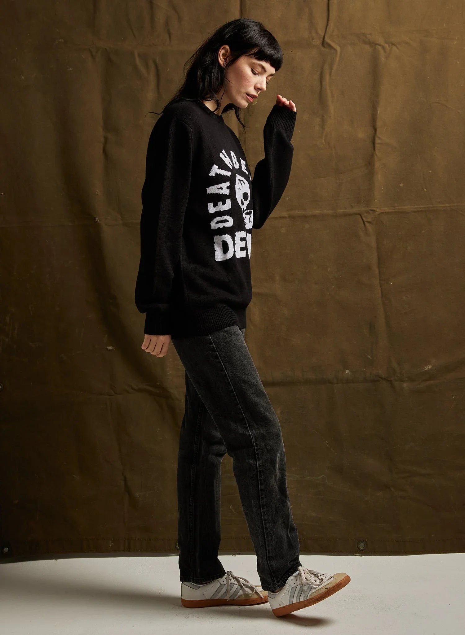 Woman wearing black Death Before Decaf sweater with skull design and black jeans in studio