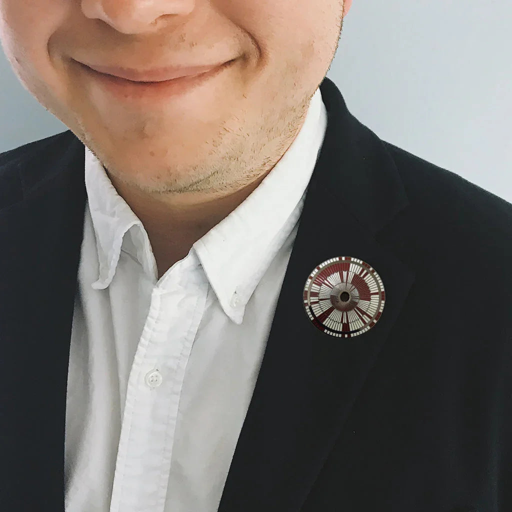 Close-up of a smiling man in white shirt and black blazer wearing a steampunk gear lapel pin