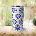White travel tumbler with blue floral tile pattern on wooden table with blurred green background