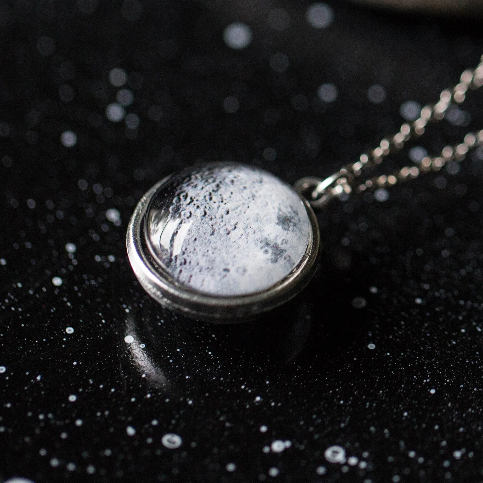 Close-up of a round moon surface pendant necklace on a starry black background