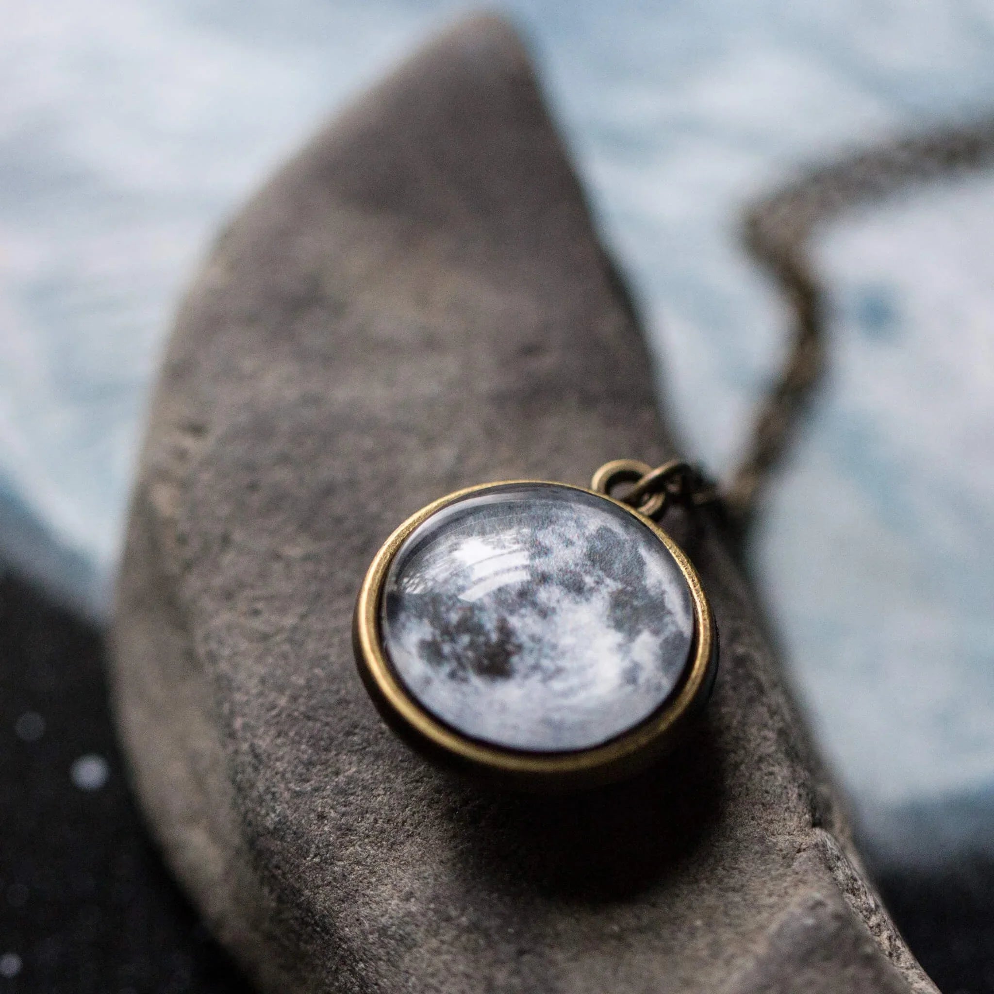 Round pendant necklace with moon image on textured surface and blurred background