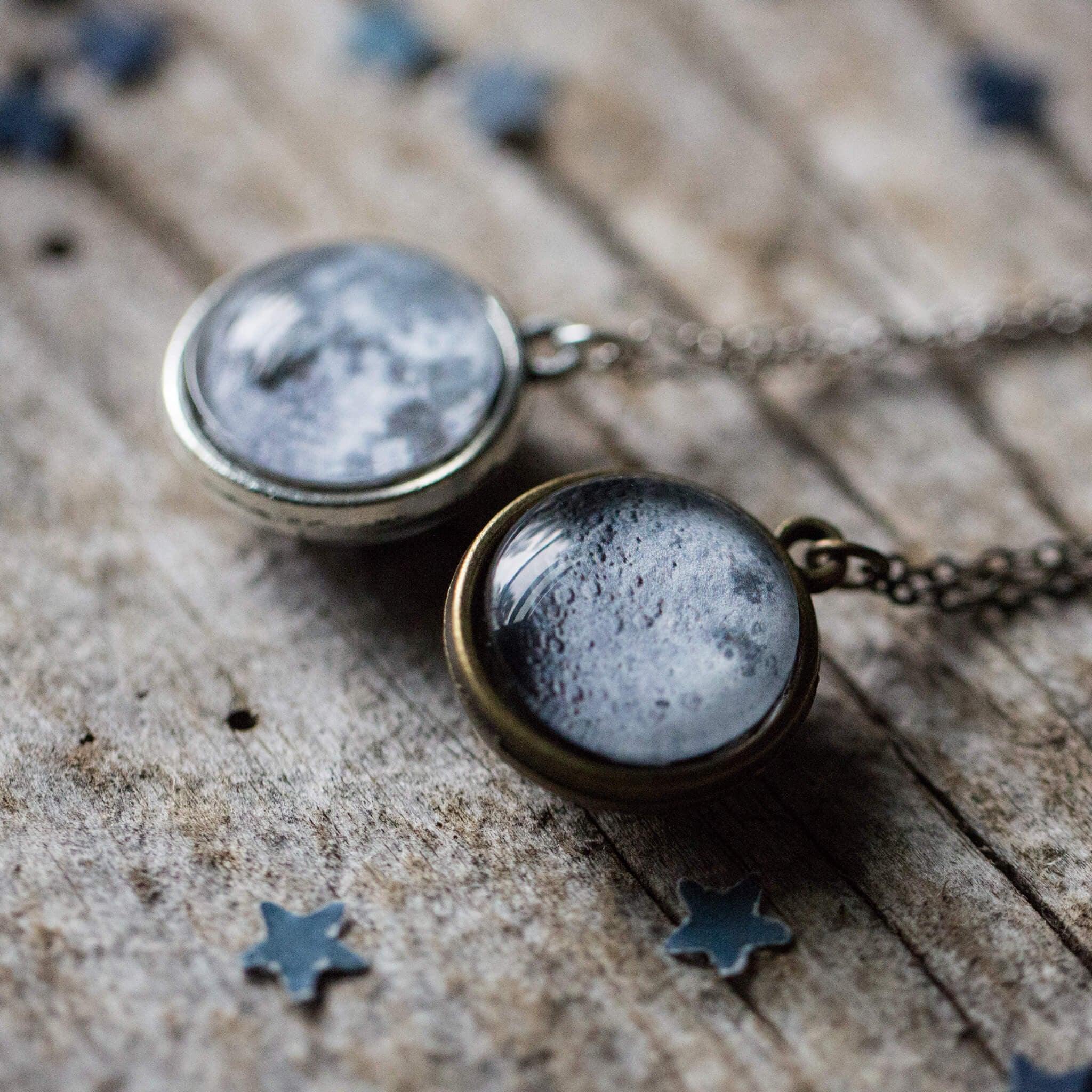 Two moon-themed pendant necklaces on a rustic wooden surface with small star confetti