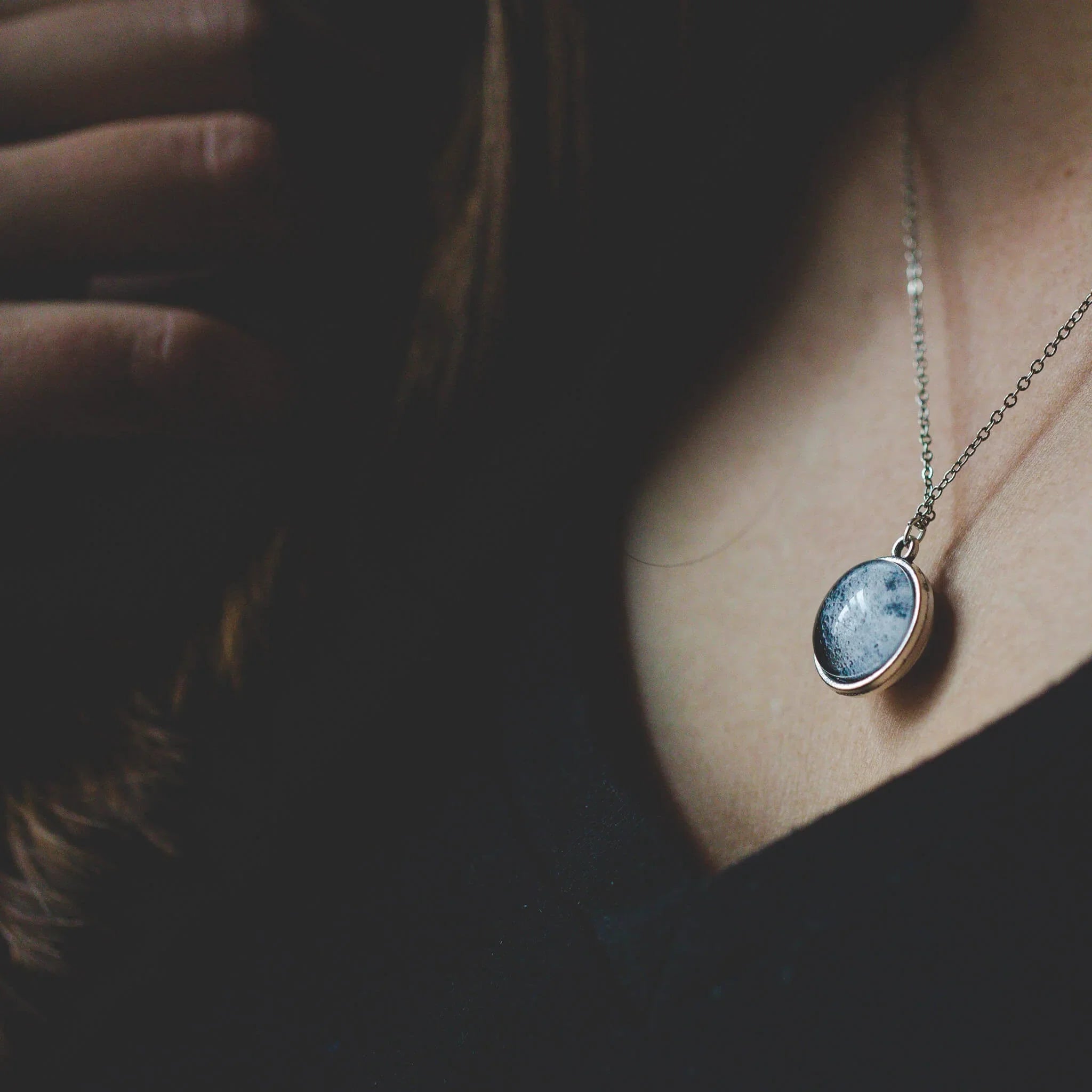 Close-up of a woman wearing a silver chain necklace with a round blue pendant and black top