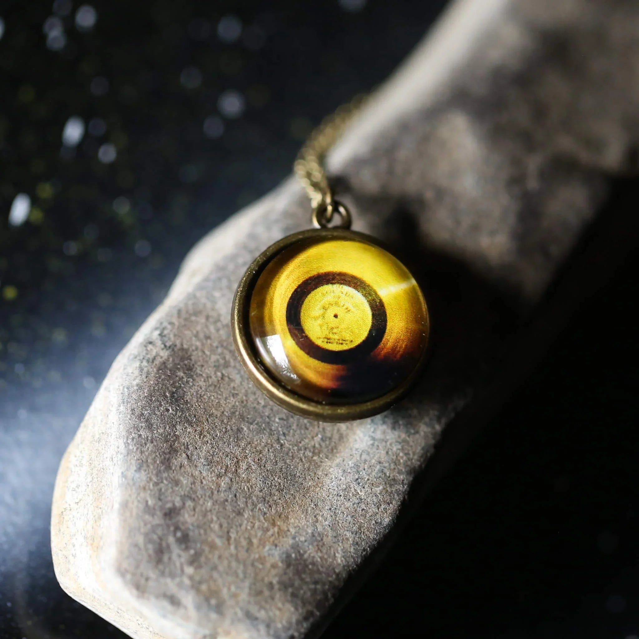 Close-up of a round amber and gold pendant necklace resting on a textured stone against a black background