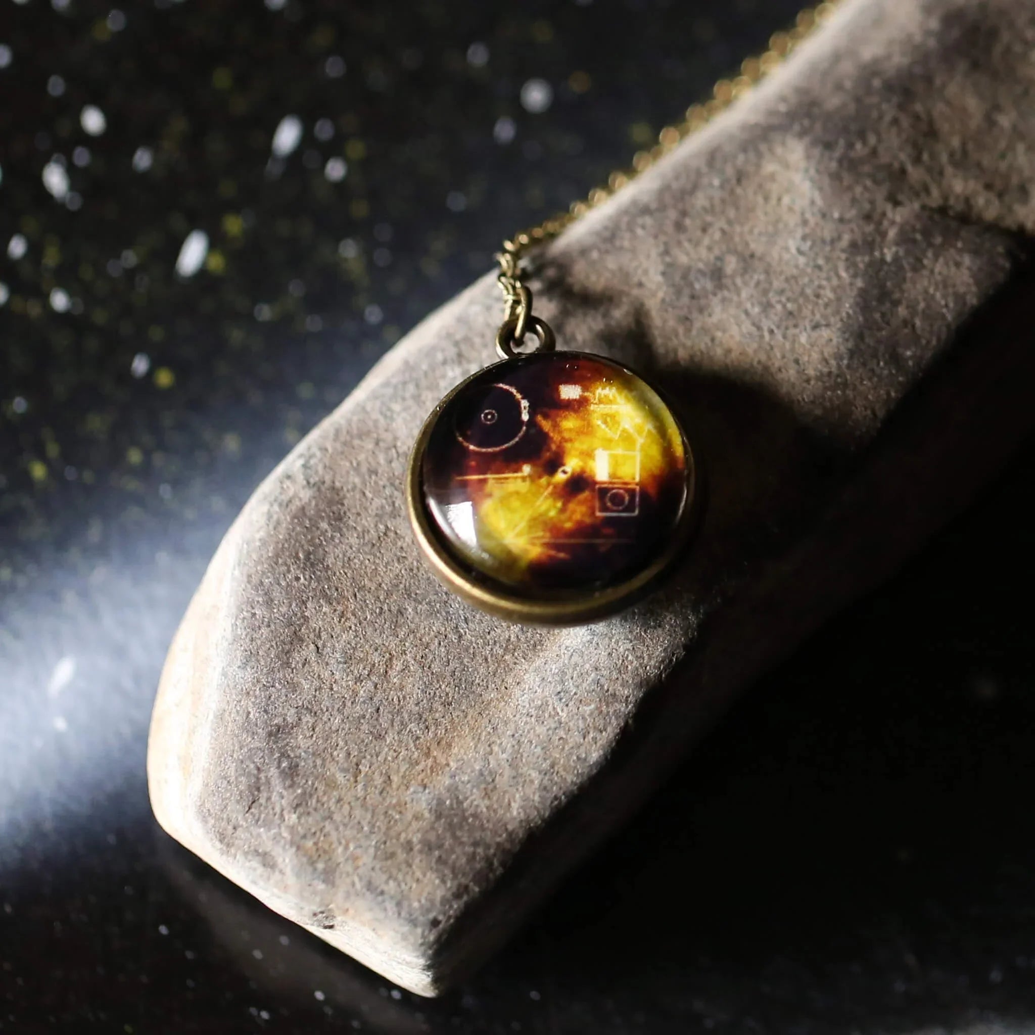 Vintage-style round pendant necklace with golden yellow and dark brown design on stone surface