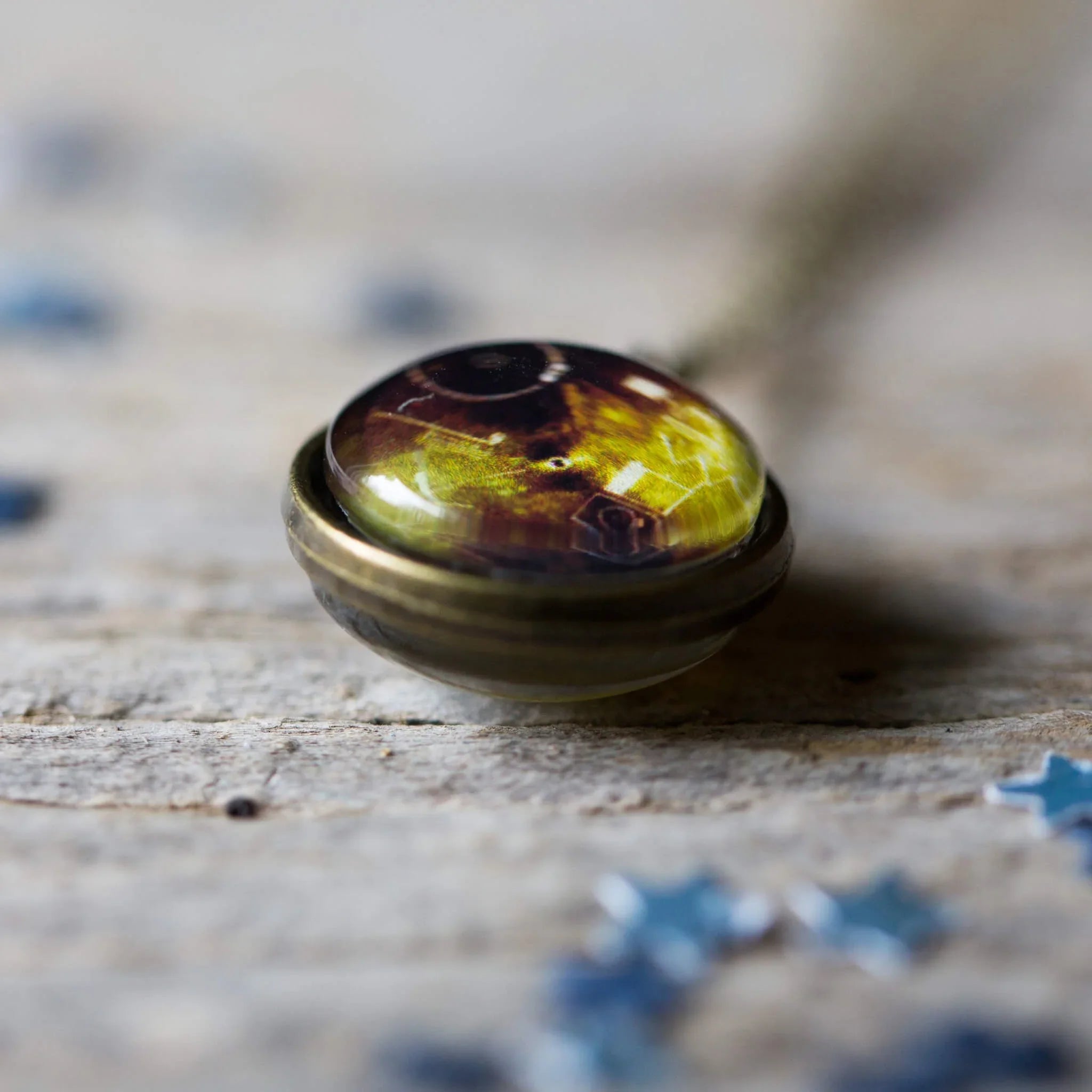 Close-up of round brass pendant necklace with glossy, amber-toned glass dome detail on wooden surface