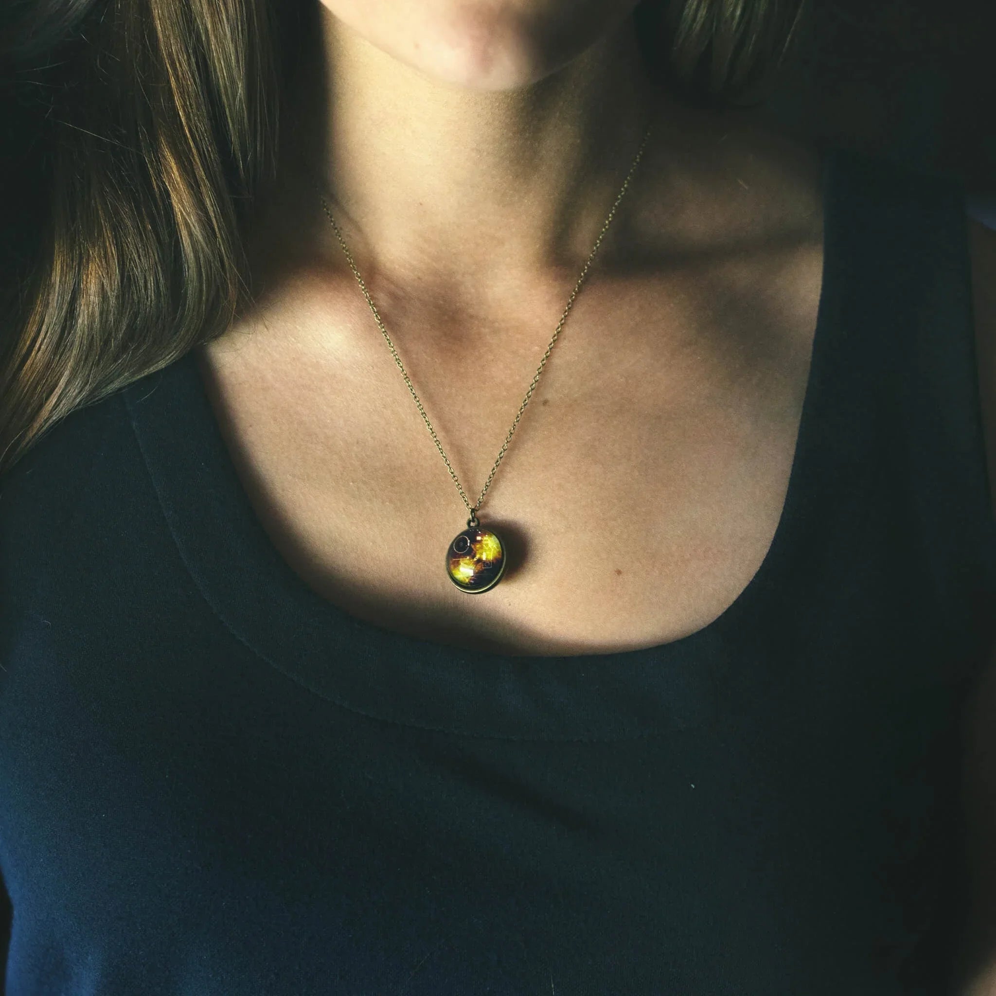Woman wearing a gold chain necklace with a glowing round pendant over a black top