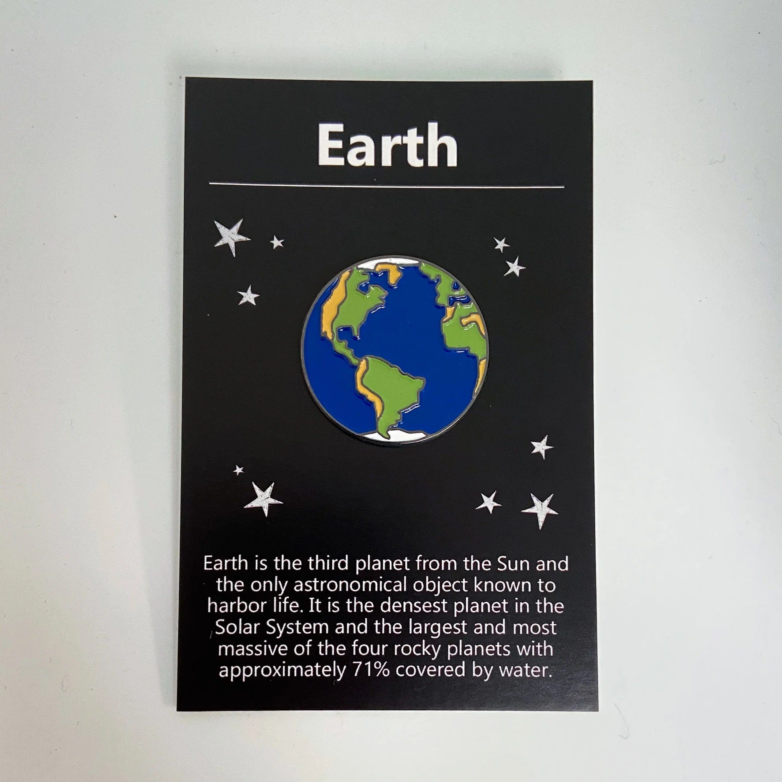 Educational Earth pin on black card with stars and text about Earth's features and water coverage