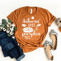 Rust orange t-shirt with white autumn-themed print, folded jeans, cotton stems, and striped flats on white background