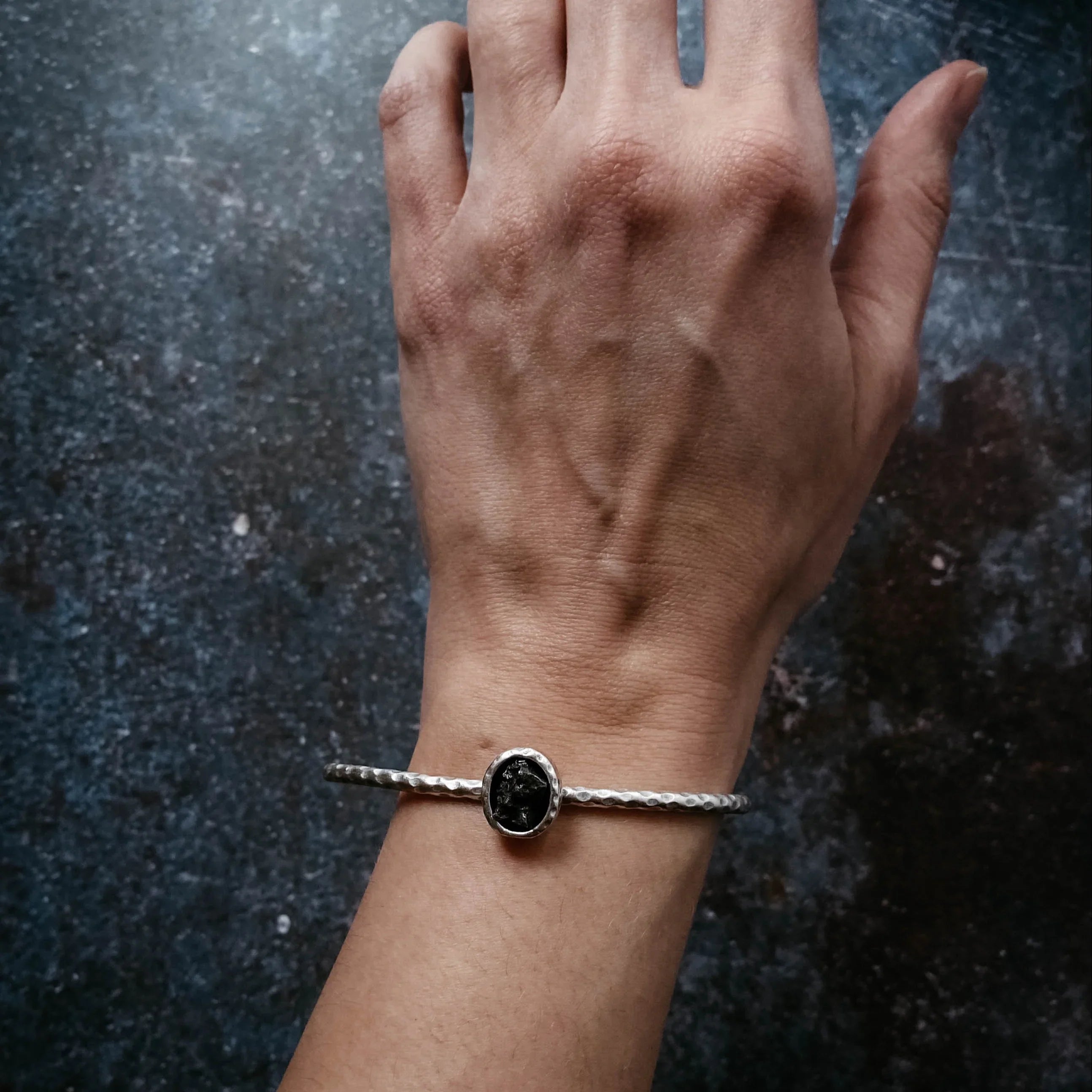 Hand wearing a silver bracelet with a black stone, Qu!rk Boutique artist-designed jewelry