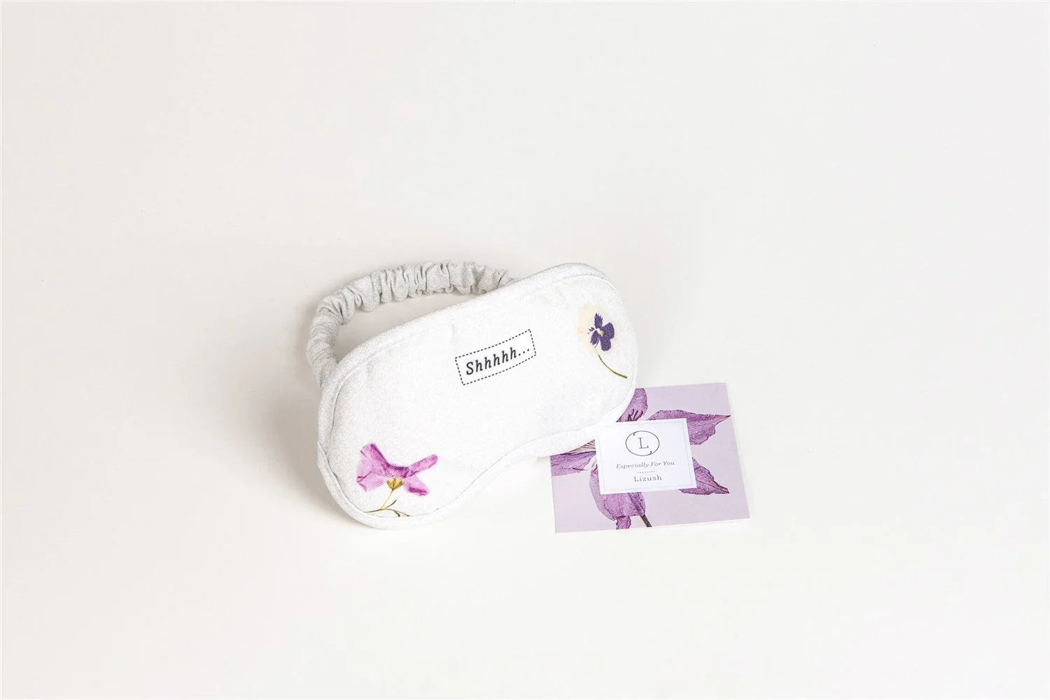 White sleep mask with purple floral accents and 'Shhhhh...' text, displayed on a lavender card