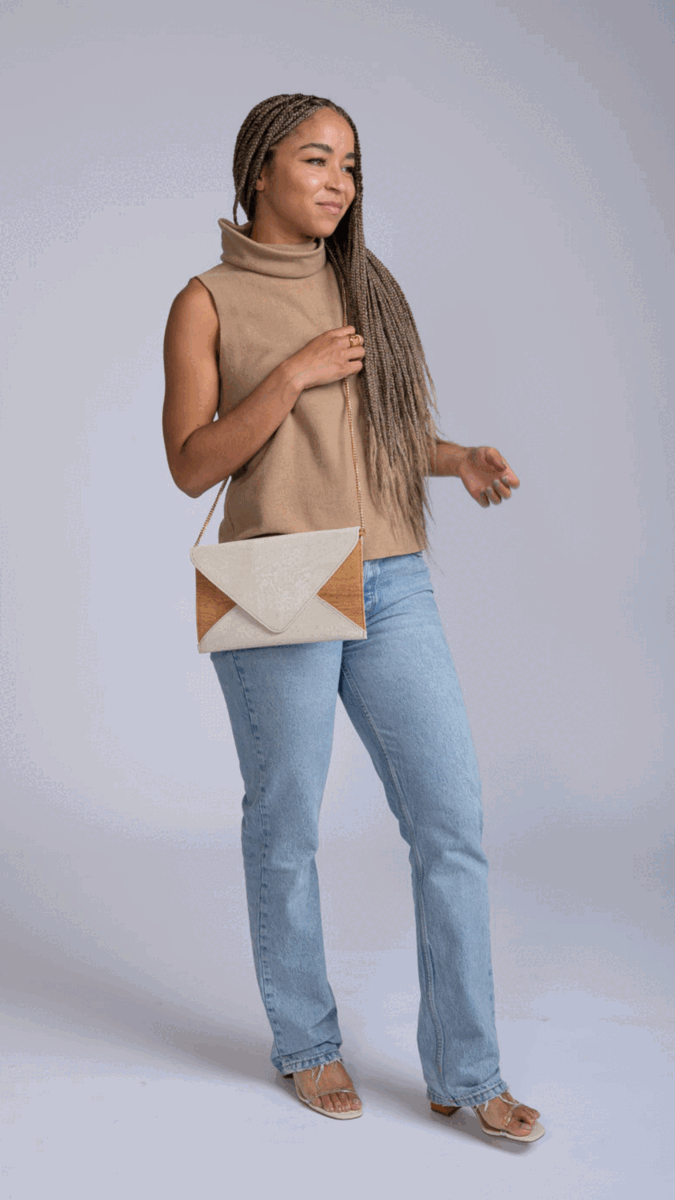 Woman modeling a modern beige sleeveless top, light wash jeans, femme-fit sandals, and a sustainable envelope clutch, promoting Qu!rk Boutique’s artist-designed cosmic couture fashion.