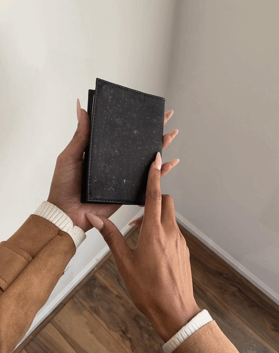 Hand holding and opening a black eco-friendly wallet on a wooden floor, Qu!rk Boutique gift idea