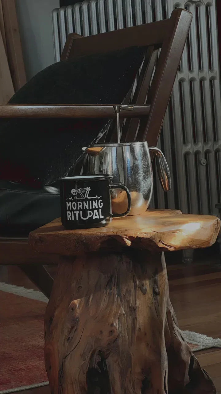 Black 'Morning Ritual' mug and silver French press on rustic wood table, cozy boutique setting