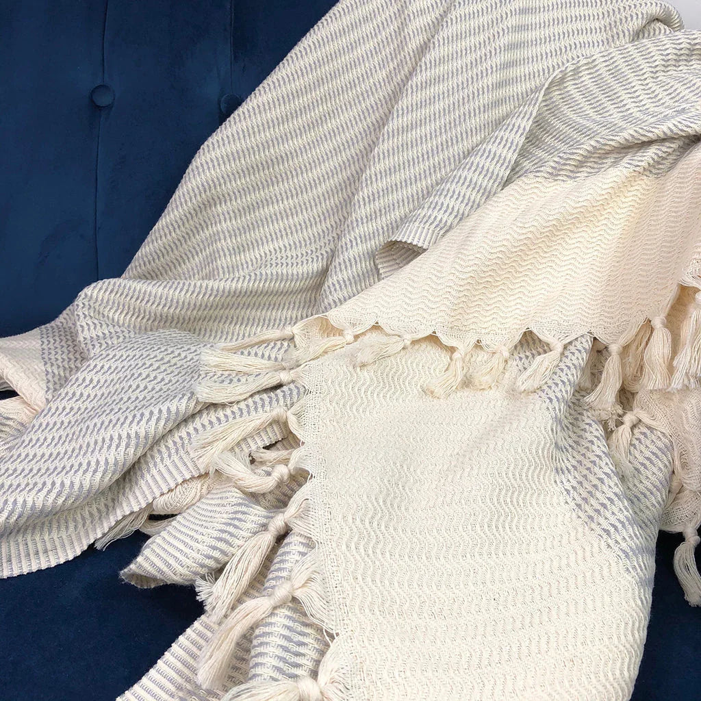 Fair trade woven cream and grey blanket with tassels draped on a blue sofa at Qu!rk Boutique