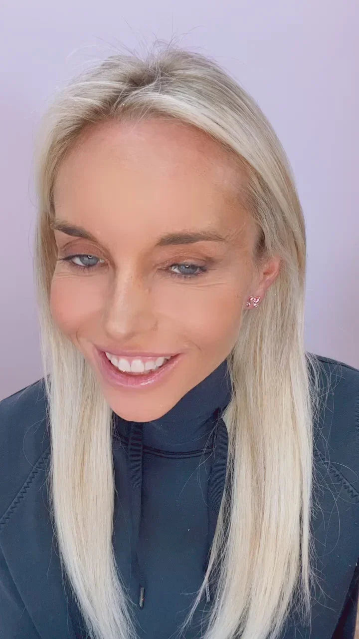 Smiling blonde woman with straight hair wearing small butterfly earrings and a dark hoodie against light background