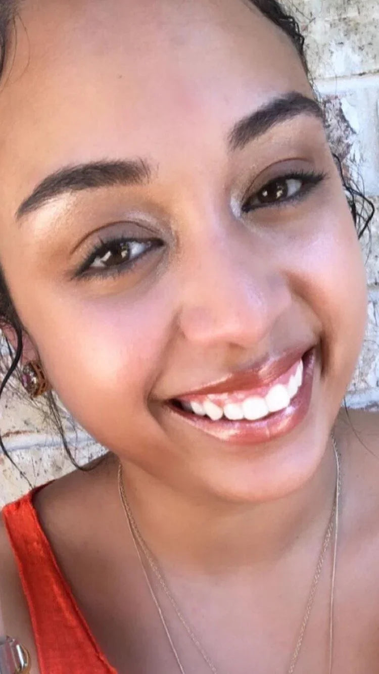 Smiling woman in orange top near textured wall, radiant and joyful, Qu!rk Boutique style.