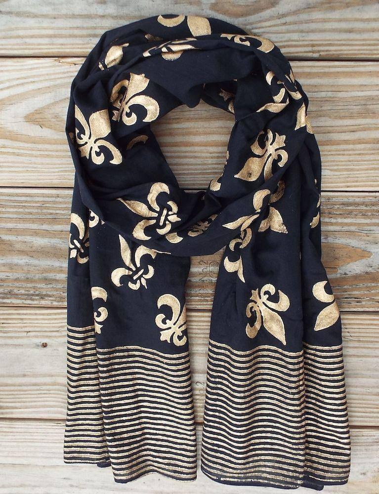 Black scarf with gold fleur-de-lis print and striped border, displayed on wood background