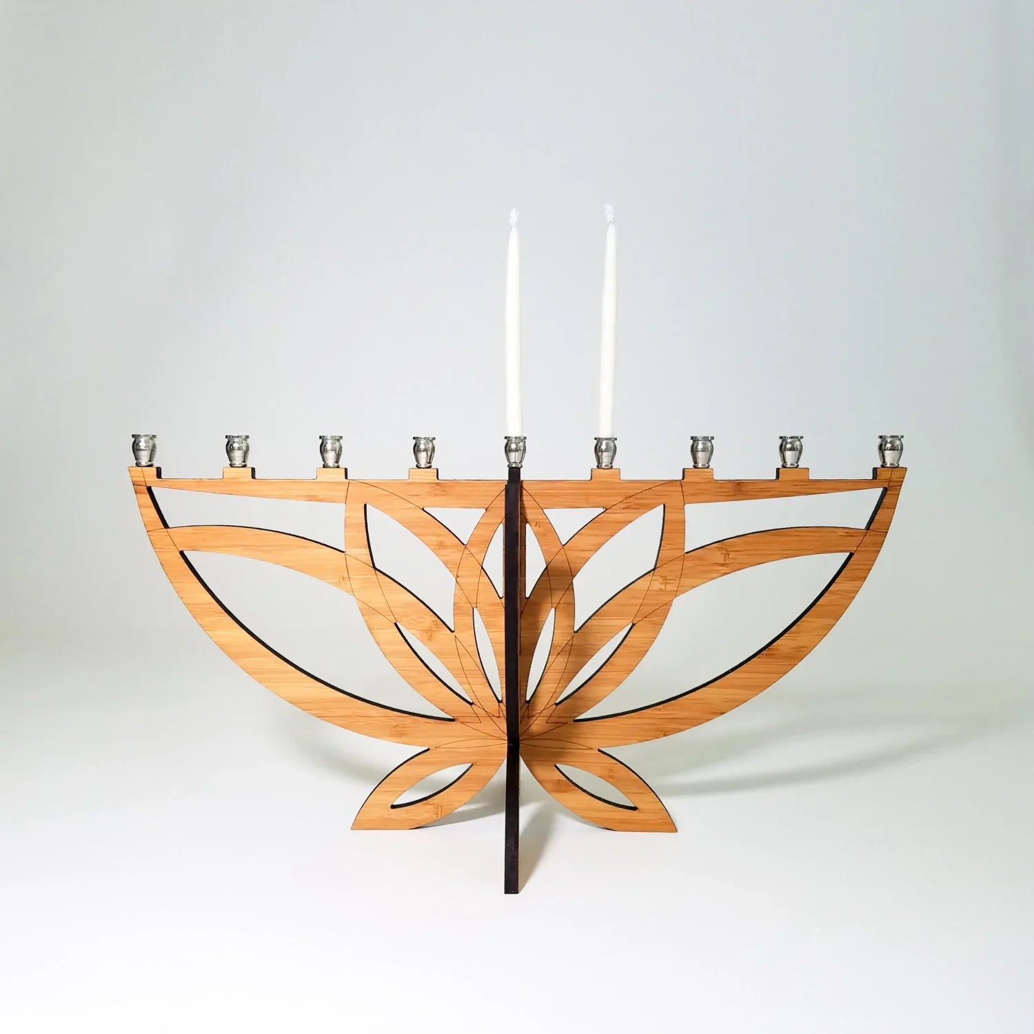 Modern wooden menorah with geometric cutouts and two white candles on a white background