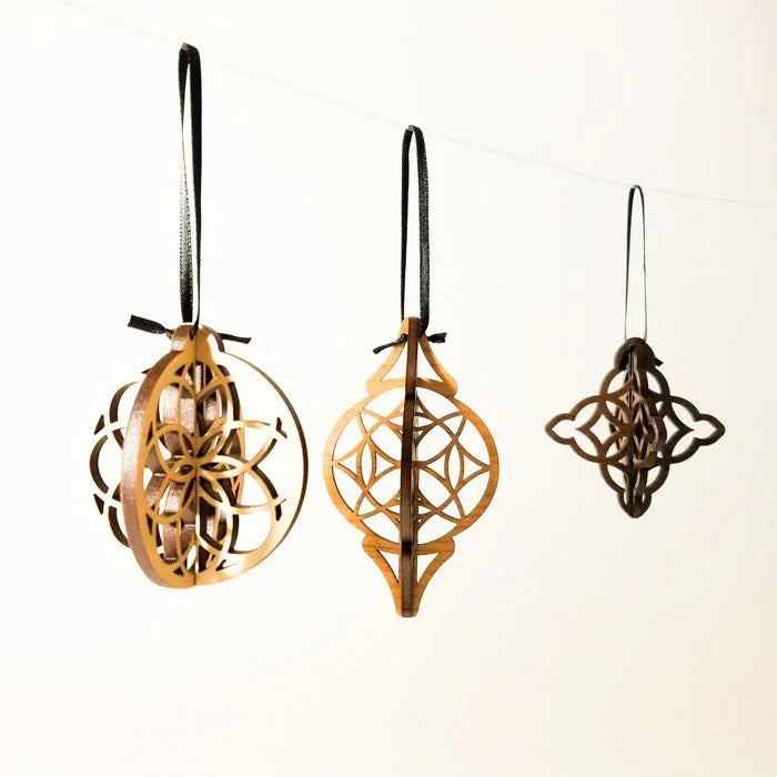 Modern laser-cut wood Christmas ornaments set with geometric designs, hanging on black ribbons.