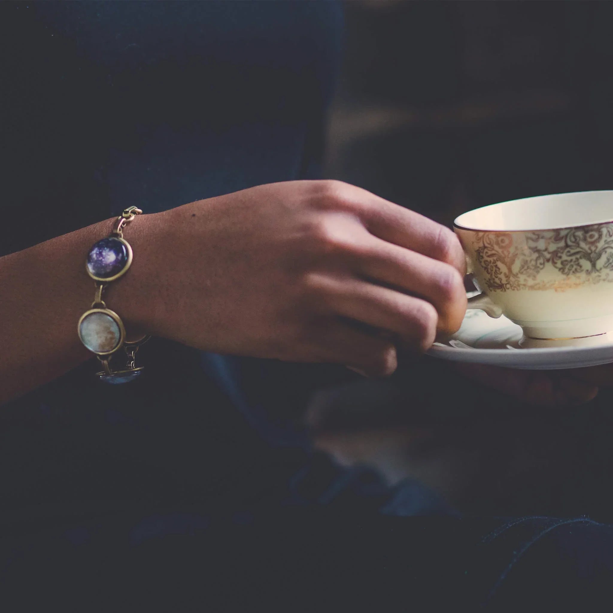 Woman wearing cosmic bracelet holding vintage teacup, Qu!rk Boutique artist-designed jewelry