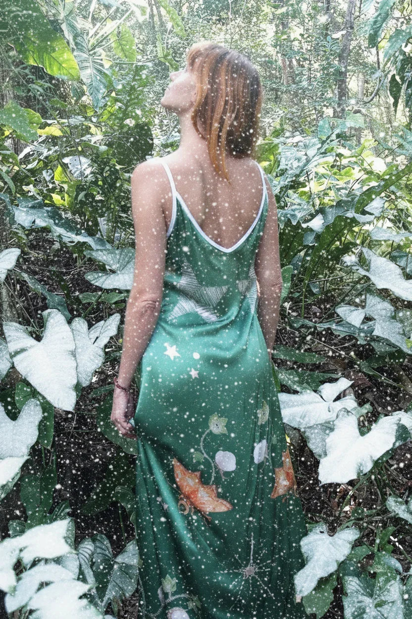 Woman in green floral maxi dress standing in lush green foliage with a snowfall effect
