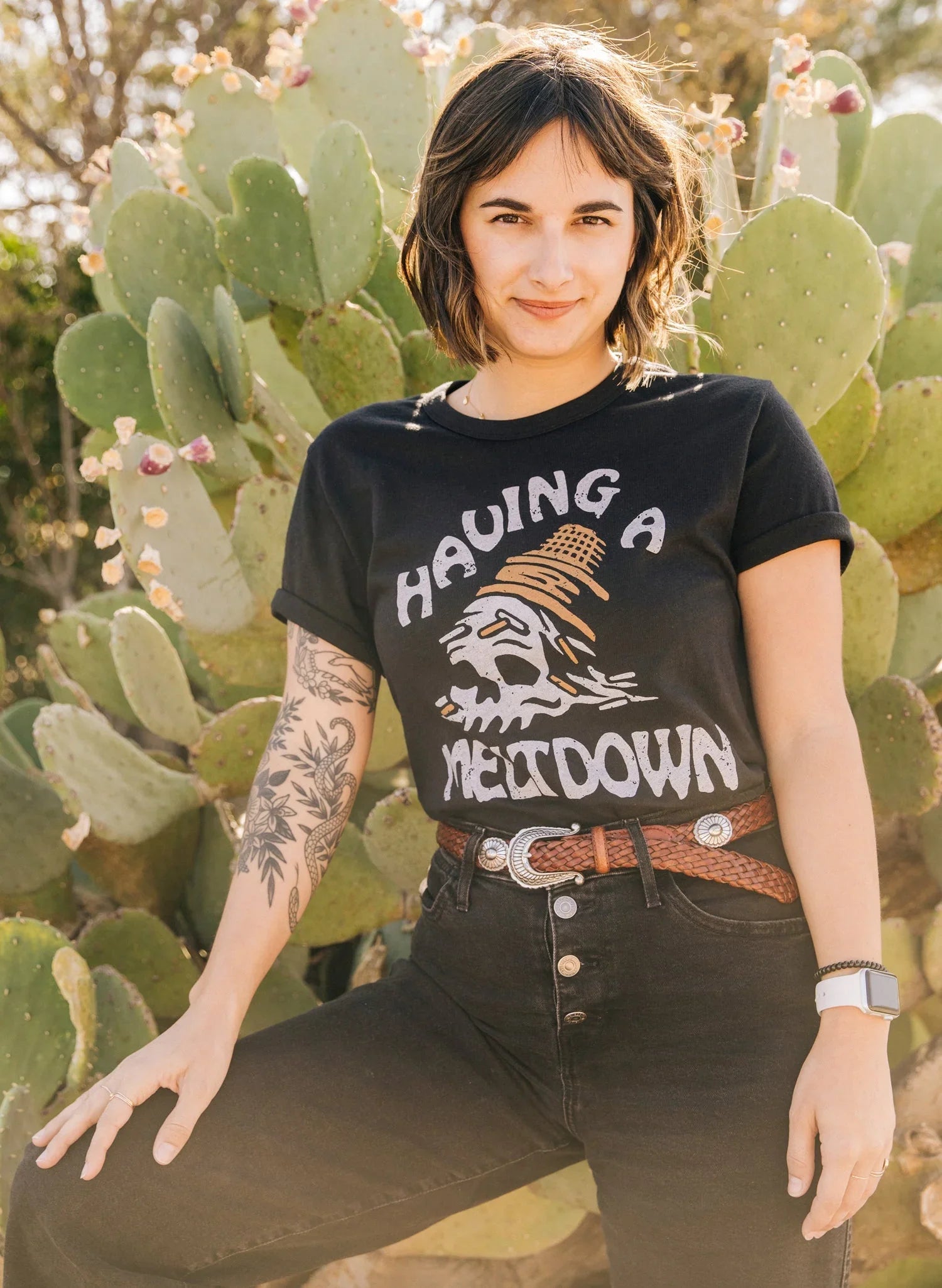 Woman in black graphic t-shirt with meltdown text and cactus background, casual style with tattoo and watch