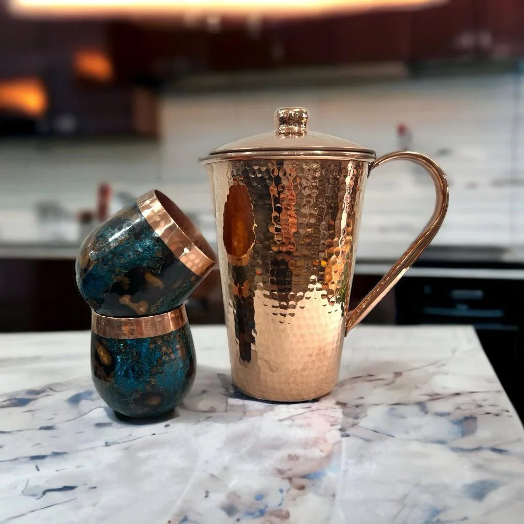 Hammered copper jug with lid and two blue-gold tumblers on marble counter at Qu!rk Boutique