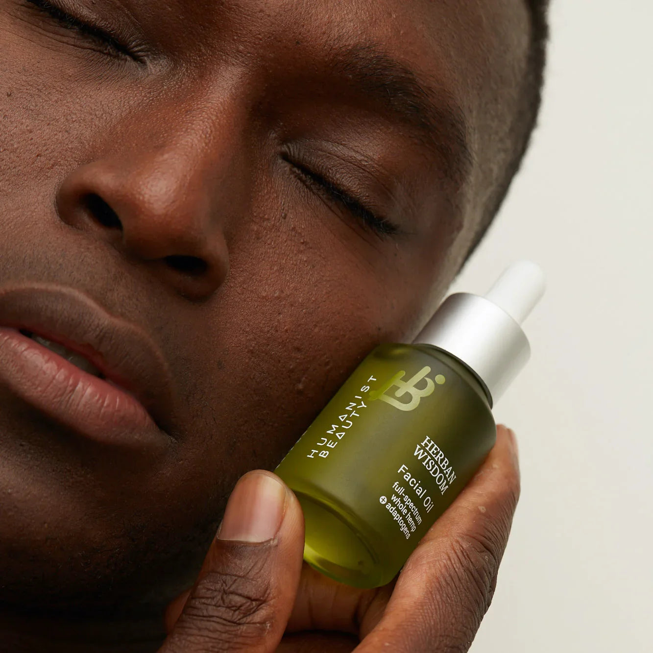 Person with closed eyes holding Humanist Beauty Herban Wisdom Facial Oil by face, skincare product