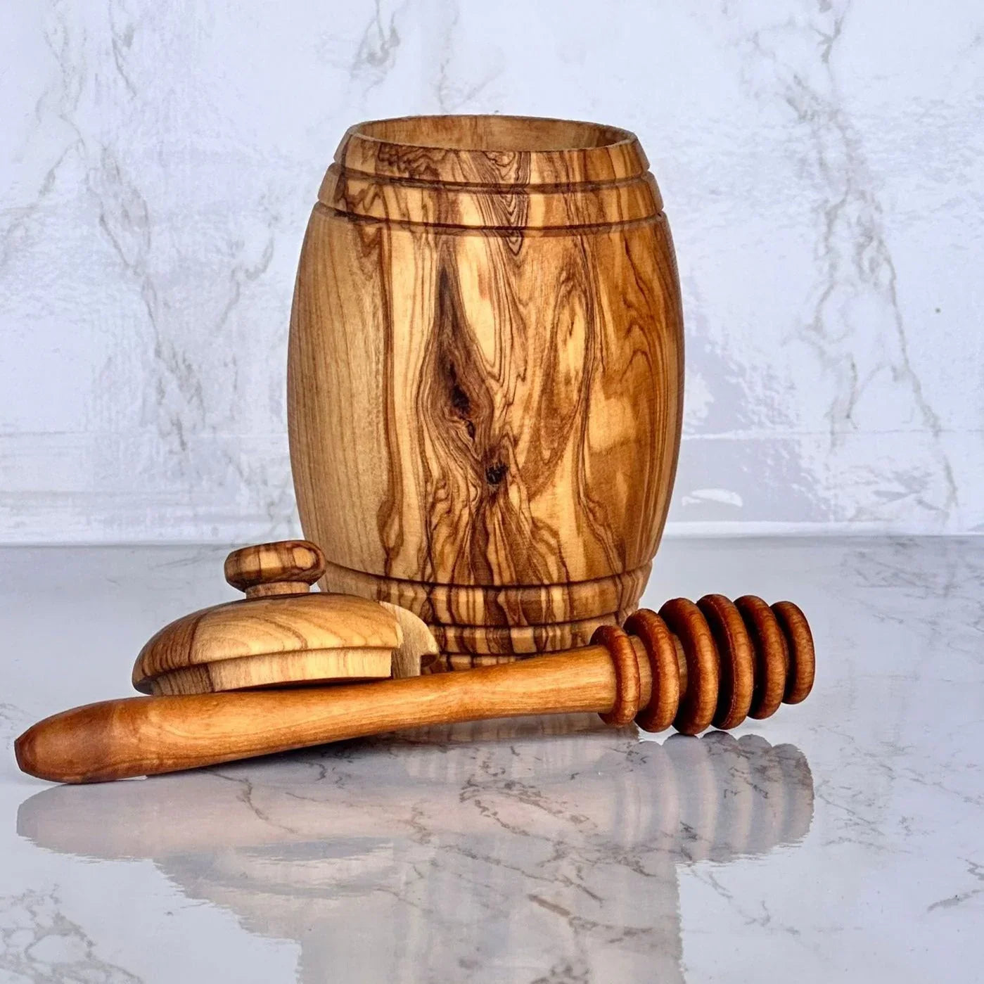 Wooden honey pot with lid and honey dipper on a marble surface