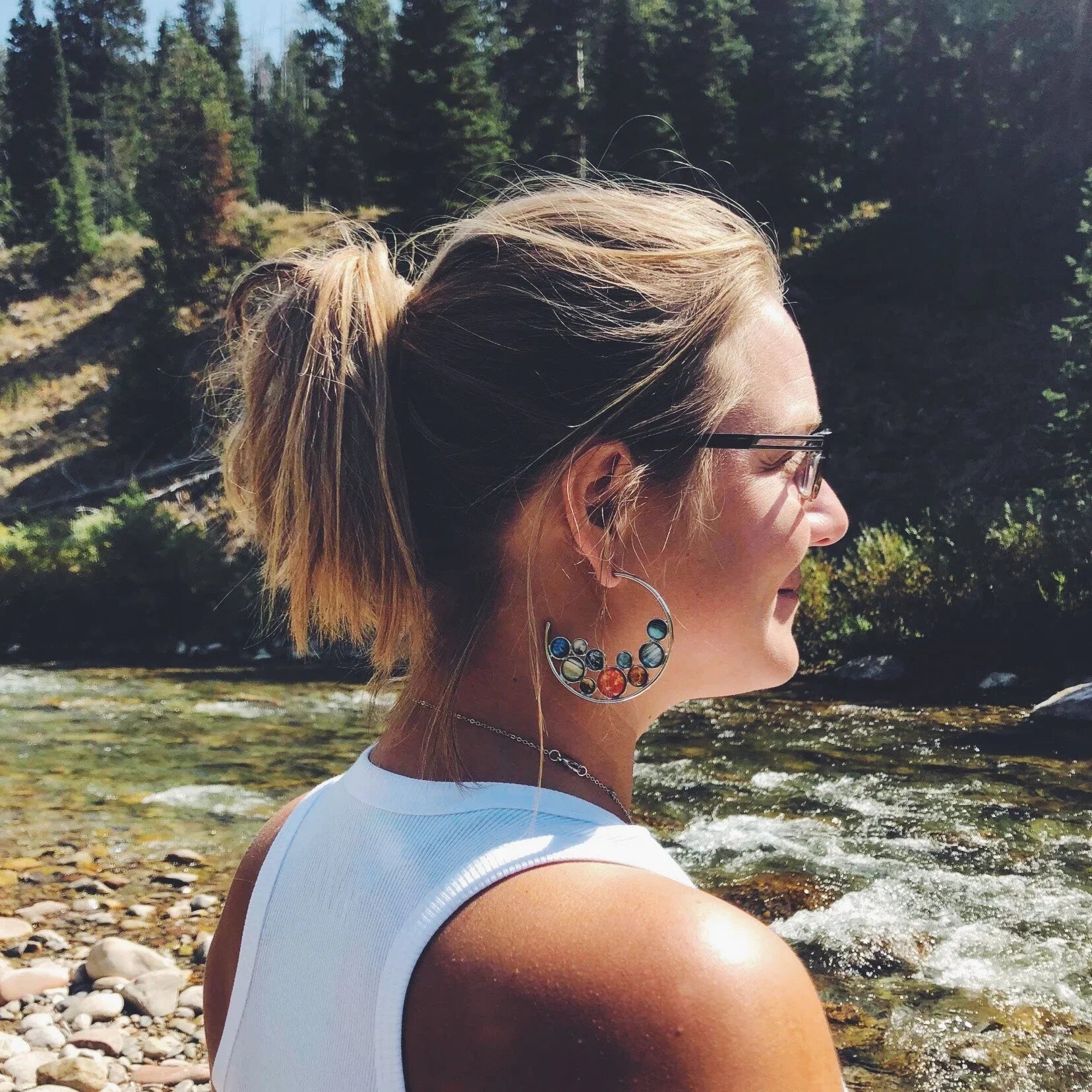 Woman outdoors wearing cosmic solar system hoop earrings by a river, Qu!rk Boutique