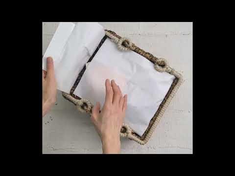 Hands placing white tissue paper inside a rectangular woven basket on a light surface