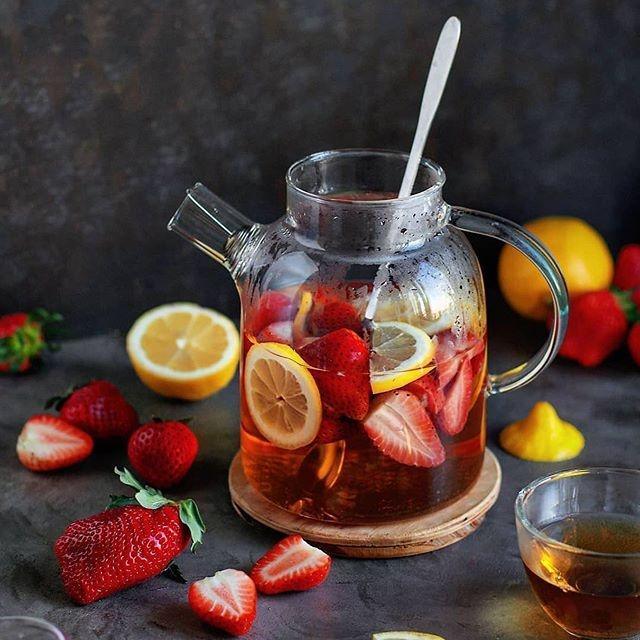 Glass teapot with strawberry lemon tea, fresh strawberries and lemons on grey table