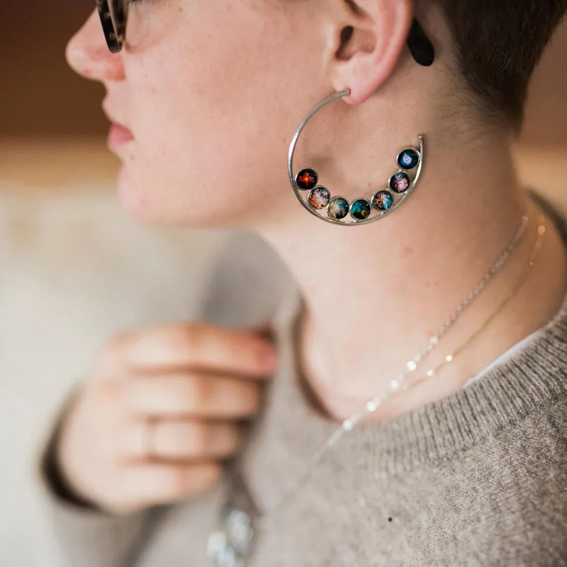 Close-up of person wearing large silver hoop earring with colorful galaxy planet charms