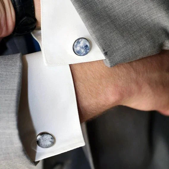 Close-up of a man's wrist wearing white dress shirt cuff with moon-themed cufflinks under a grey suit sleeve