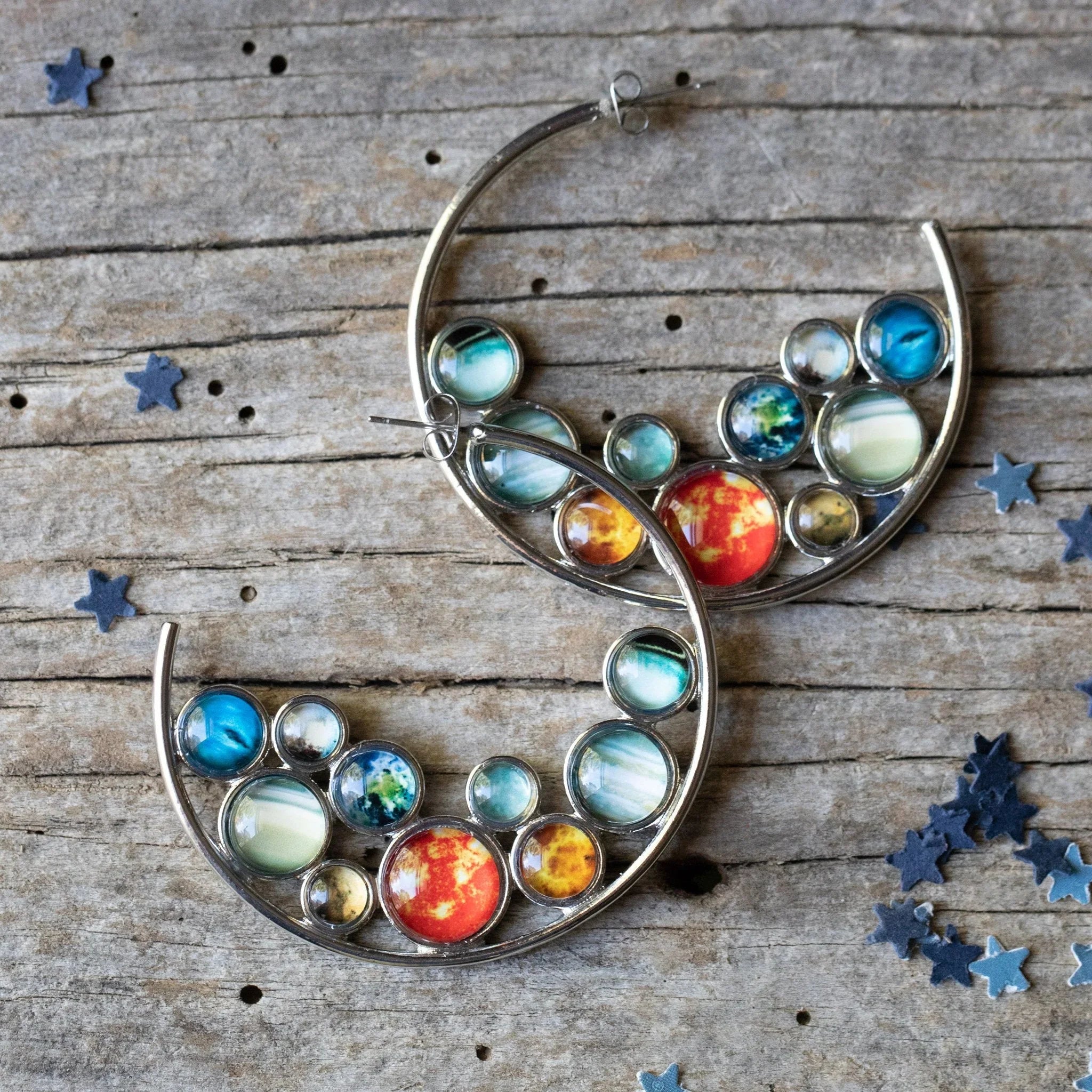 Colorful cosmic-themed hoop earrings on rustic wood, star confetti, Qu!rk Boutique jewelry