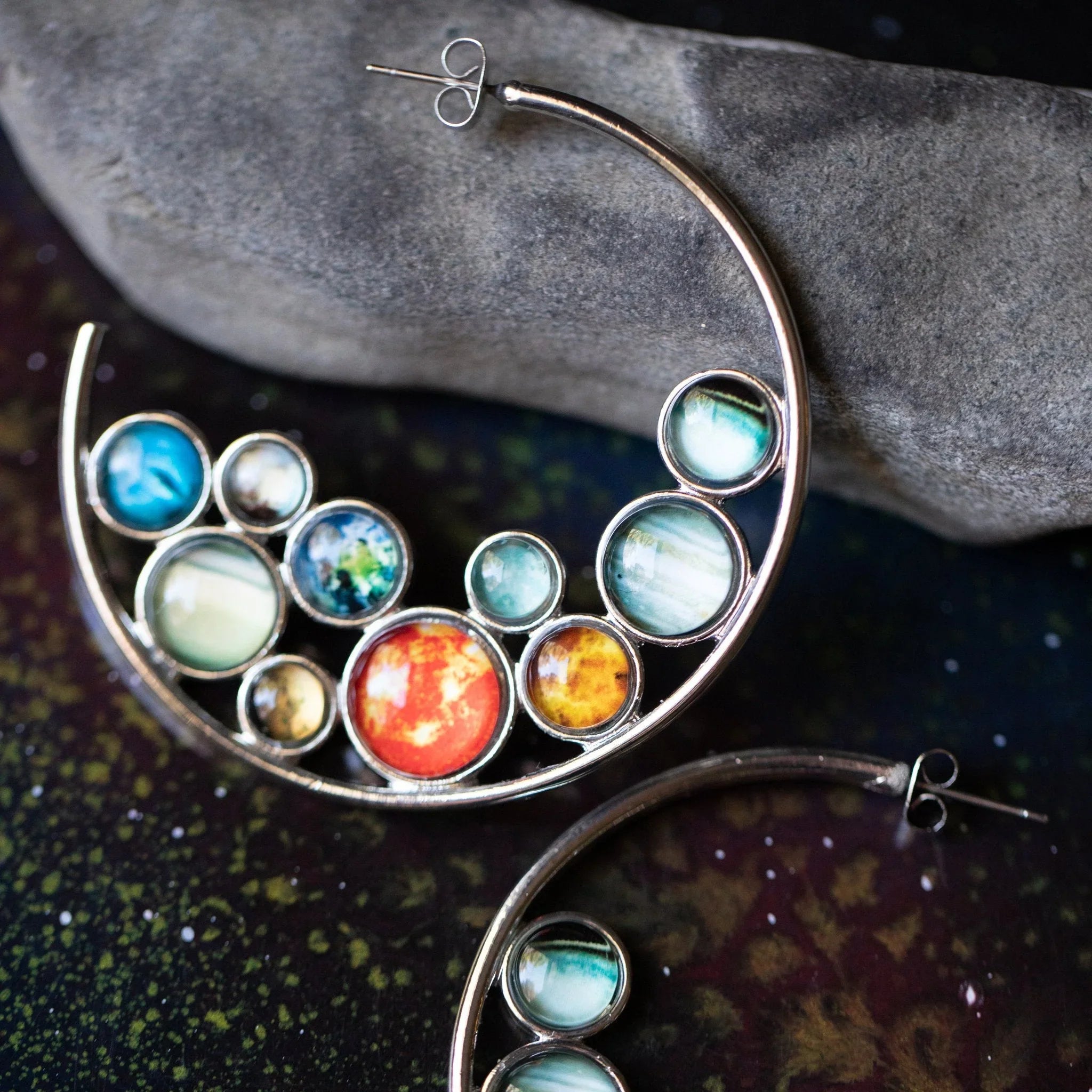 Artist-designed crescent earrings with colorful planet-inspired stones on cosmic background