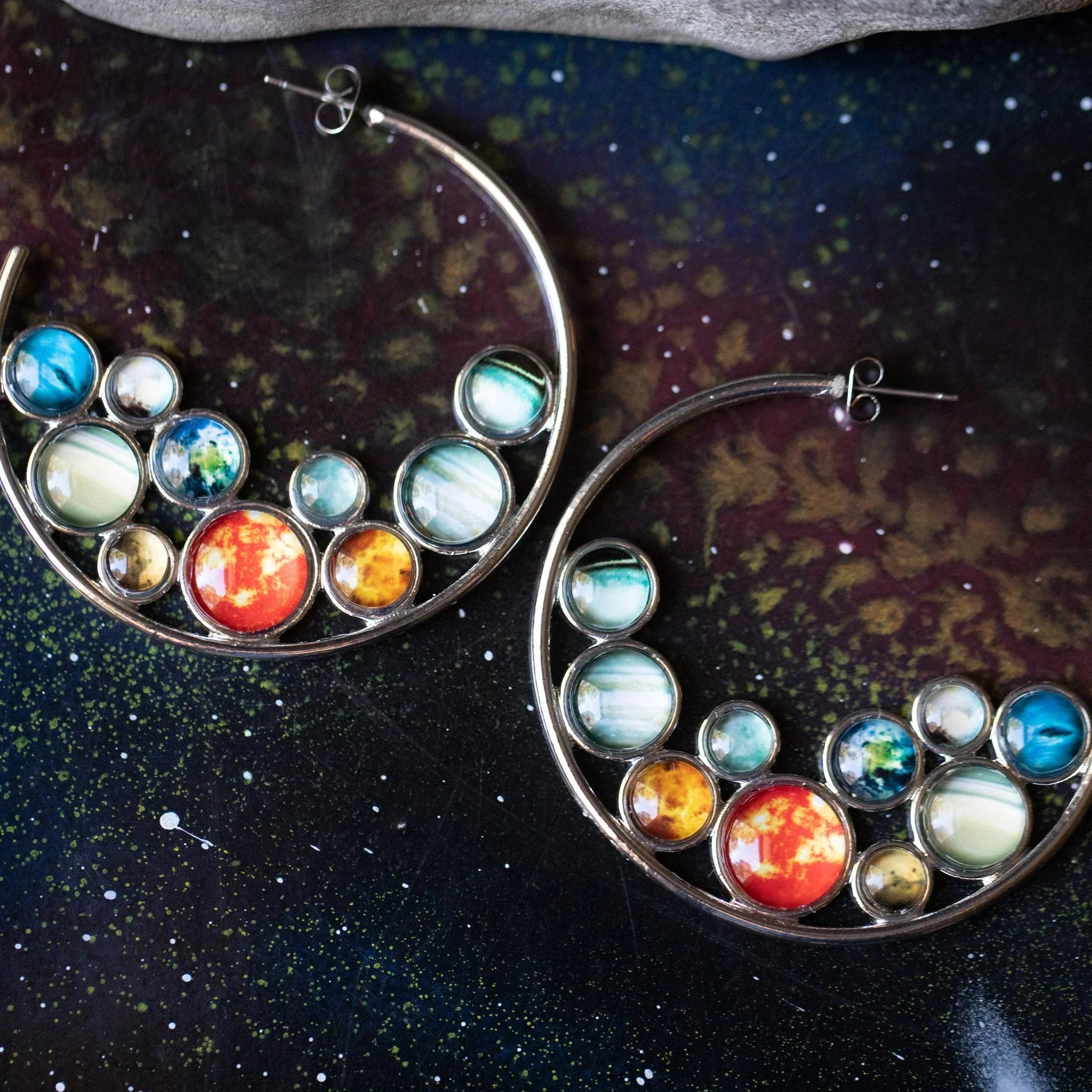 Cosmic planet hoop earrings on galaxy background, artist-designed jewelry from Qu!rk Boutique