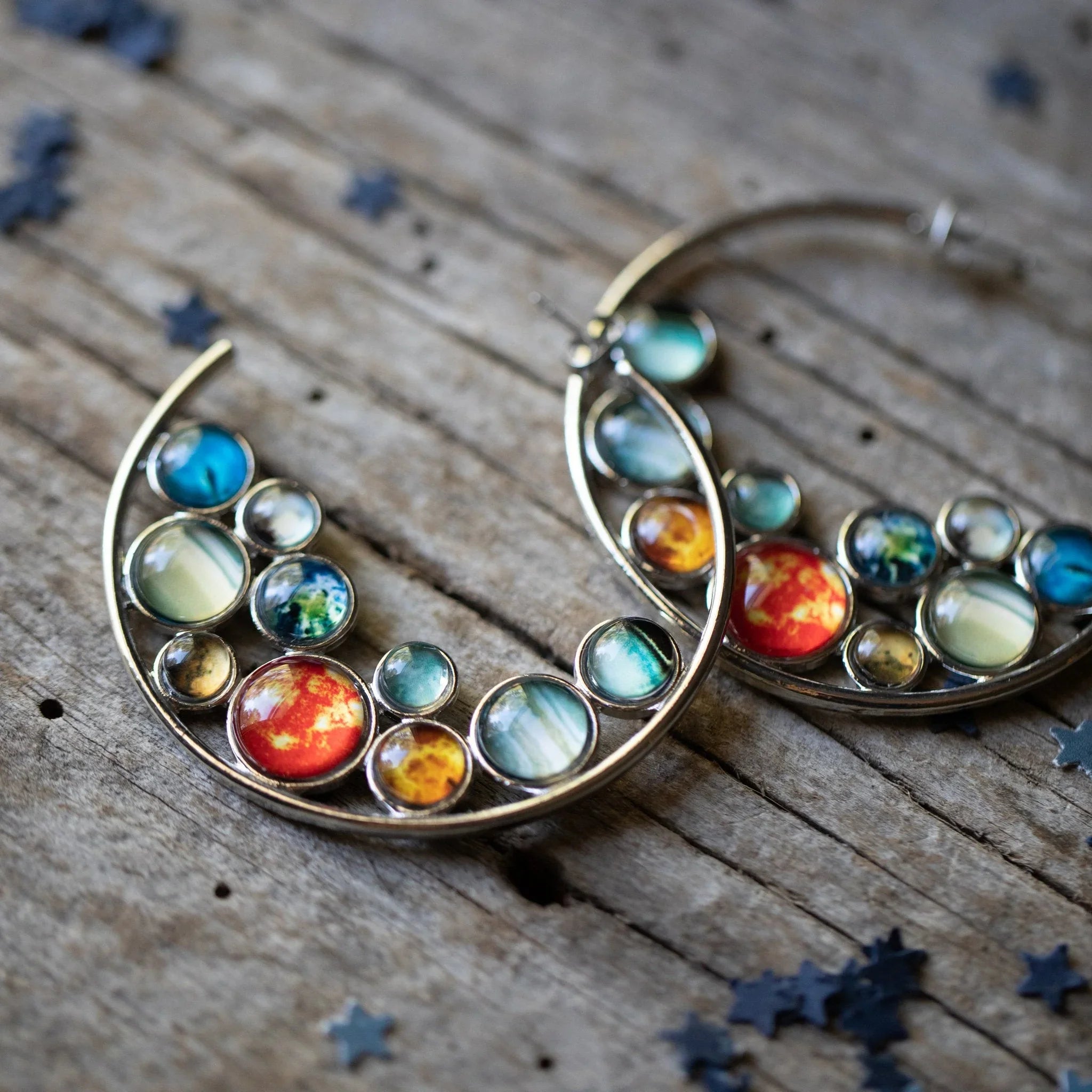 Colorful cosmic-inspired hoop earrings on rustic wood, Qu!rk Boutique artist-designed jewelry