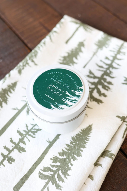 Snowy Woods soy candle tin on folded pine tree print fabric, rustic sustainable gift