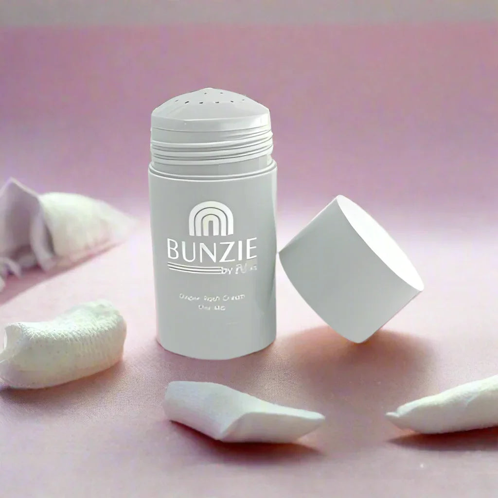 BUNZIE powder stick with open cap on pink surface, surrounded by cotton pads, at Qu!rk Boutique