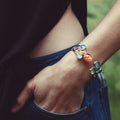 Close-up of wrist wearing a silver bracelet with colorful planet charms over blue jeans and black top