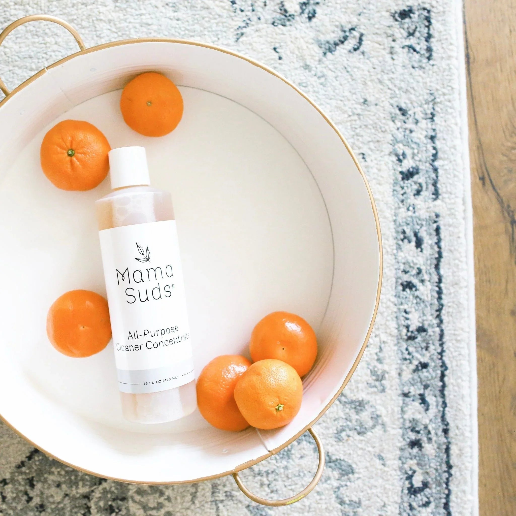 Mama Suds all-purpose cleaner with fresh mandarins in a white tray on a cozy rug