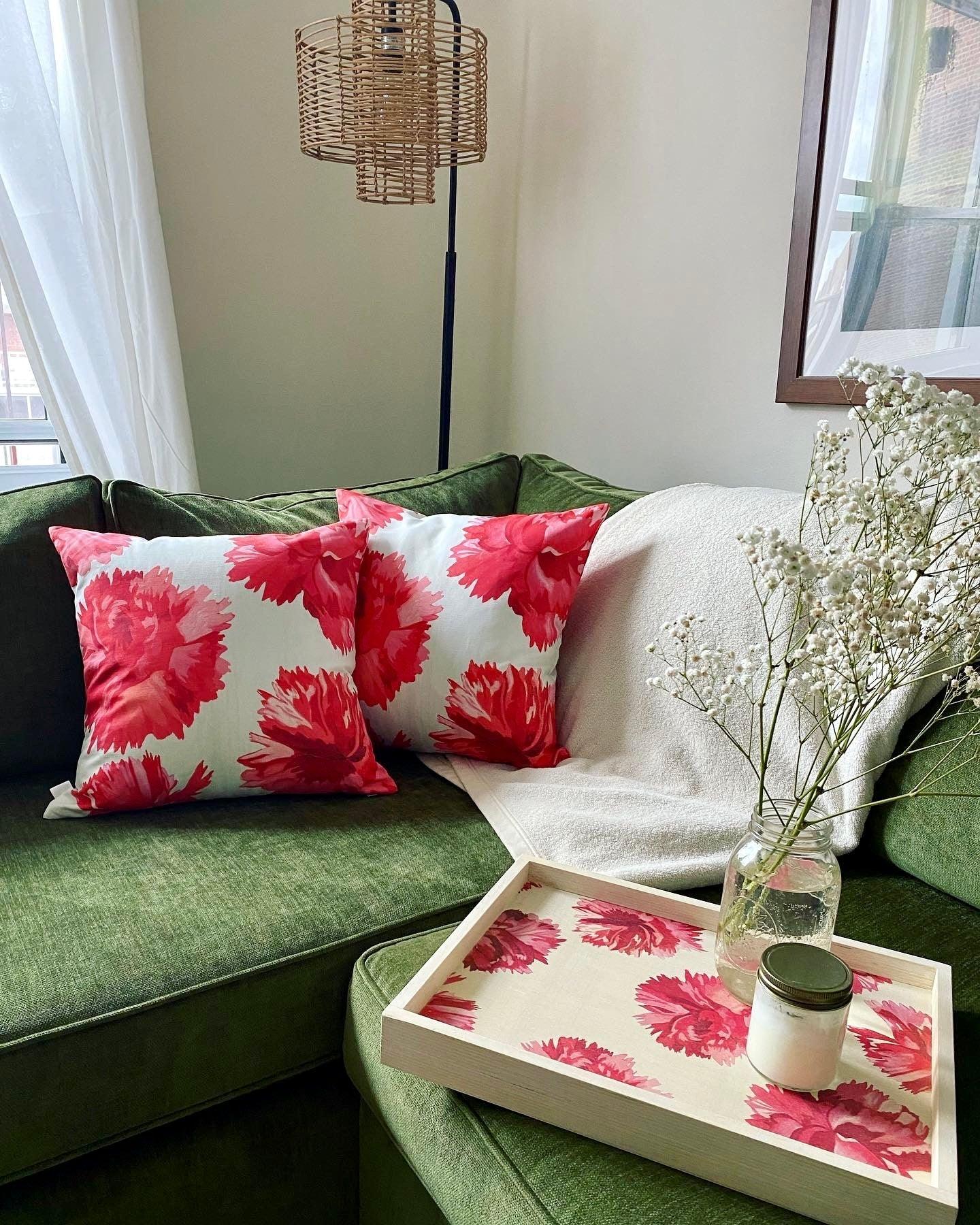 Green corner sofa with two red floral pillows, white throw, floral tray, glass jar with flowers, and candle