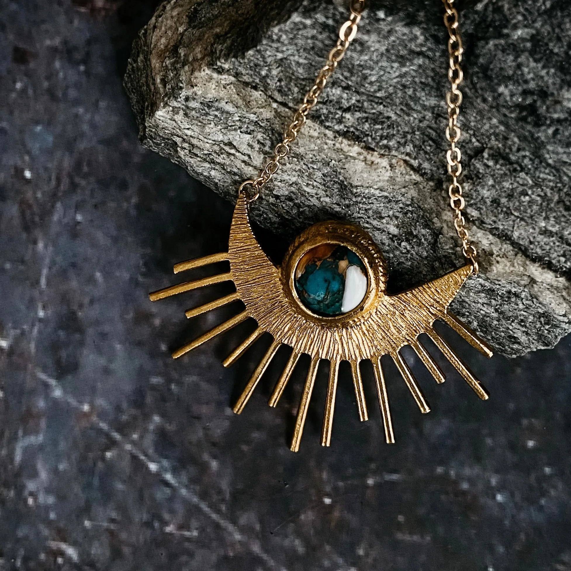 Gold sunburst necklace with turquoise and white stone pendant on textured rock
