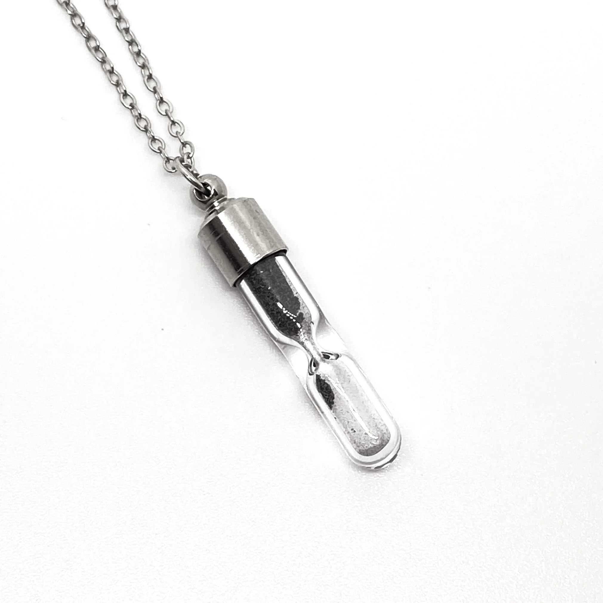 silver hourglass pendant necklace with black sand on white background